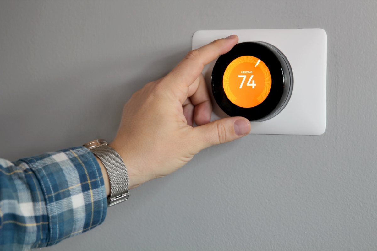 A hand turning a round smart thermostat dial set to 74 degrees in heating mode